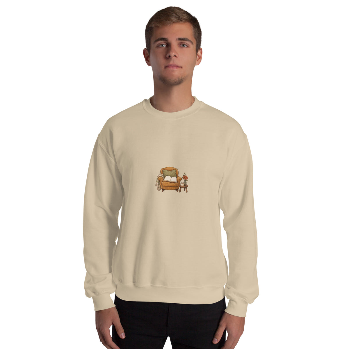Model wearing Cozy Reading Chair unisex sweatshirt in Sand, front view with armchair, open book and side table